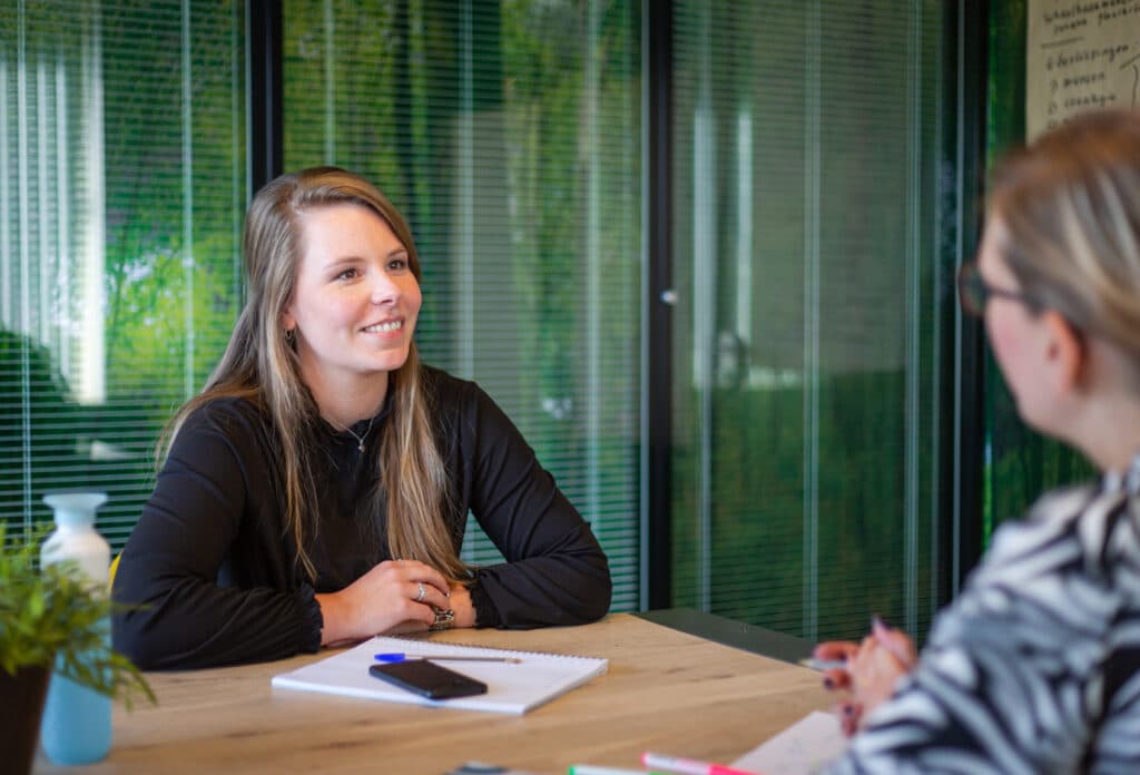 Twee personen in gesprek aan tafel tijdens overleg op kantoor