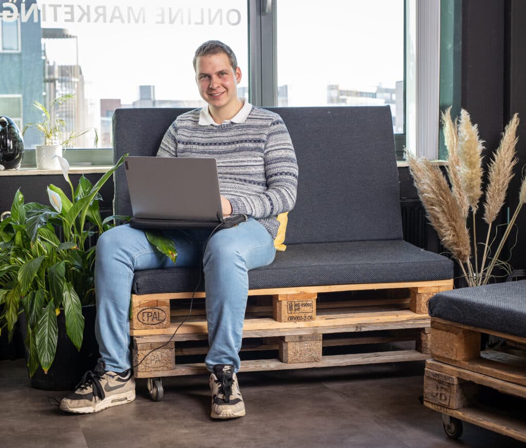 Stan, online marketeer bij Positie1, werkt met laptop op bank in kantooromgeving