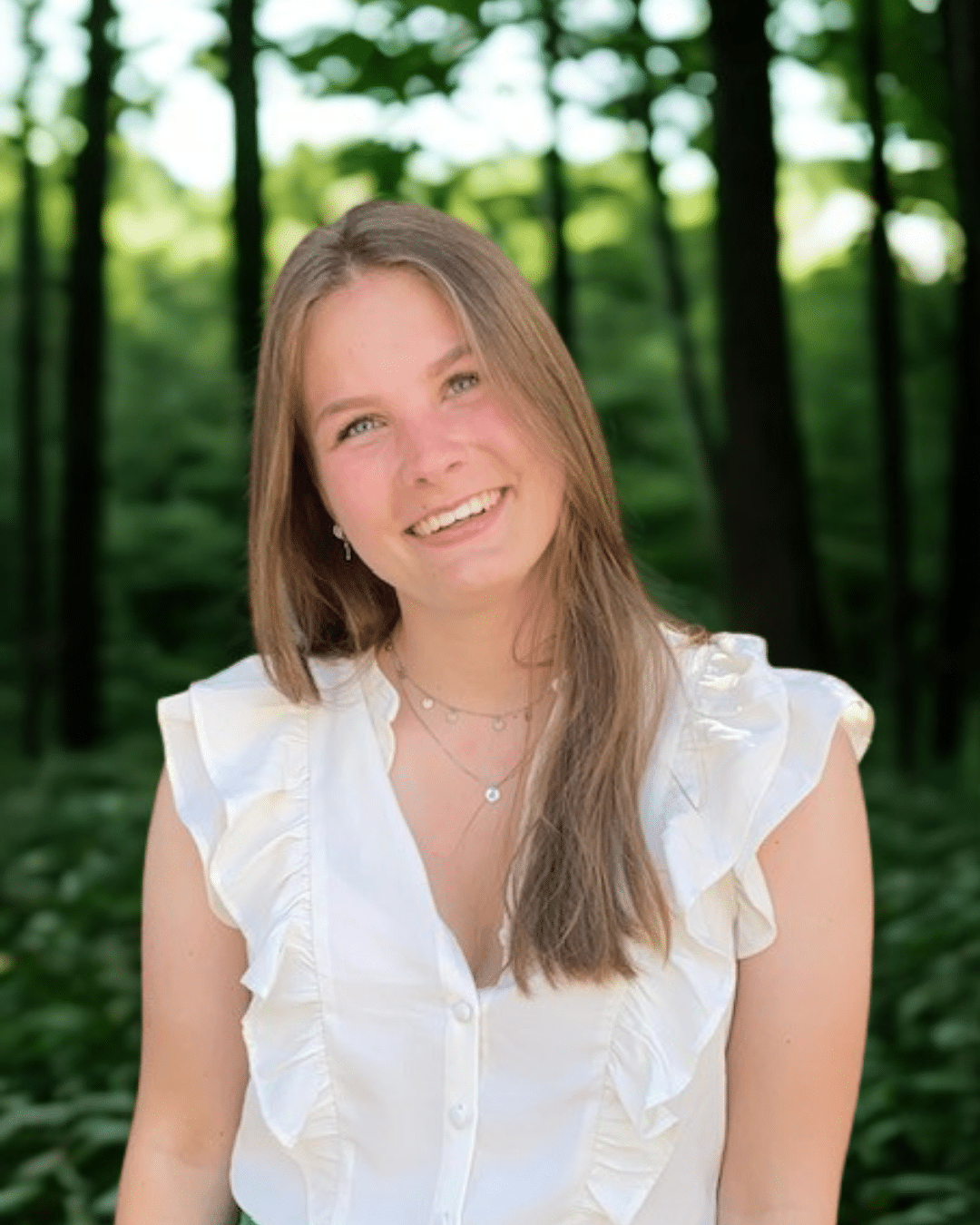 Samantha junior marketeer bij Positie1 lachend in witte blouse in groene bosrijke omgeving