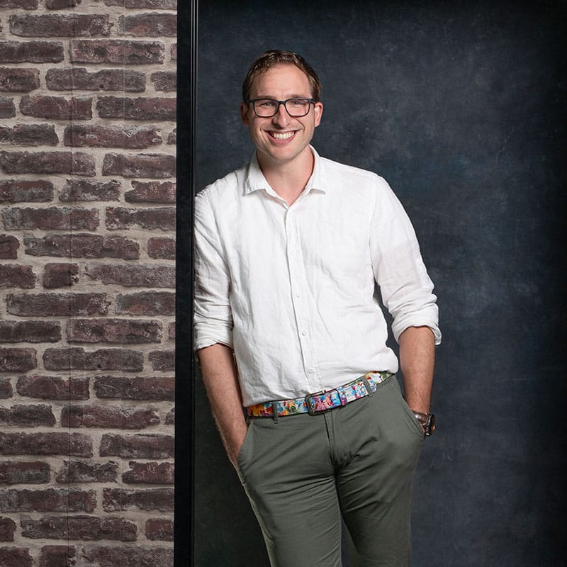 Sebastiaan projectmanager bij Positie1 staand bij bakstenen muur en donkere achtergrond